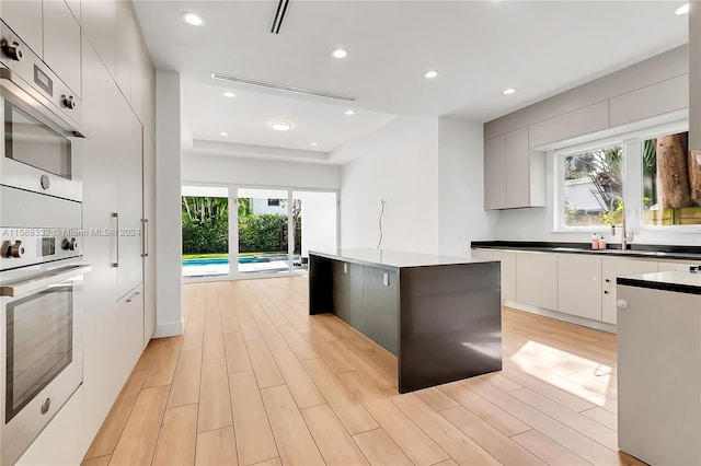 kitchen with a healthy amount of sunlight, wall oven, light wood-type flooring, and a kitchen island