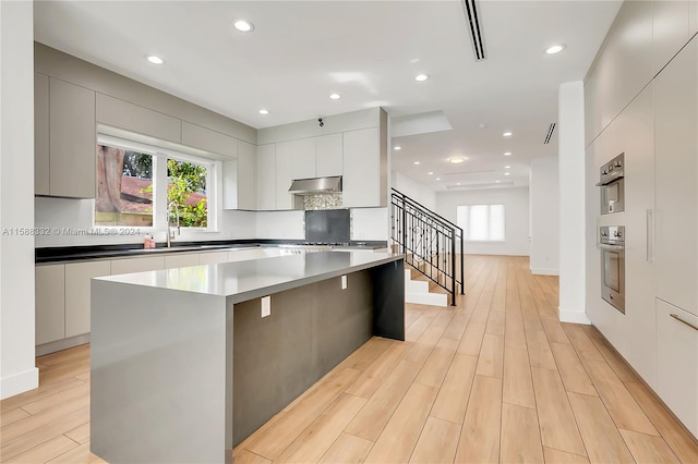 kitchen with stainless steel oven, light wood-type flooring, a kitchen island, sink, and white cabinets