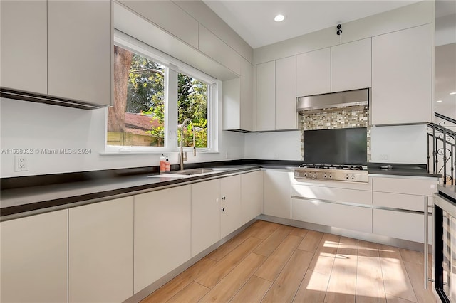 kitchen with beverage cooler, light wood-type flooring, wall chimney range hood, stainless steel gas cooktop, and white cabinets