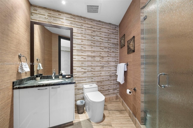 bathroom featuring tile flooring, tile walls, vanity with extensive cabinet space, a shower with door, and toilet