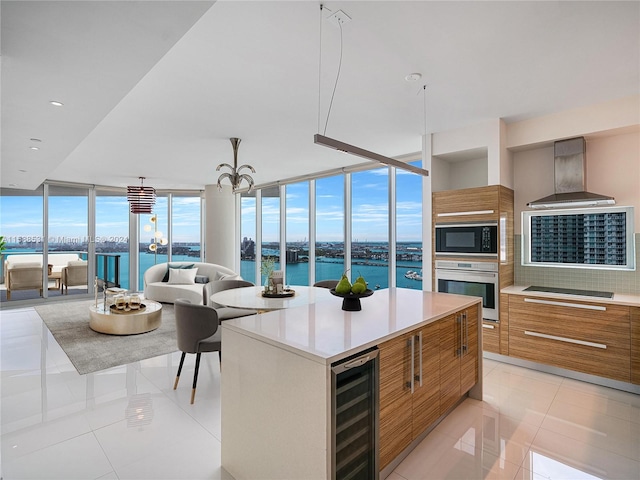 kitchen featuring wall chimney range hood, beverage cooler, black appliances, a center island, and a water view