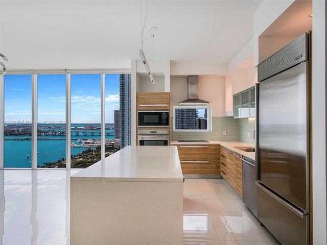 kitchen featuring tasteful backsplash, wall chimney range hood, black appliances, sink, and a water view