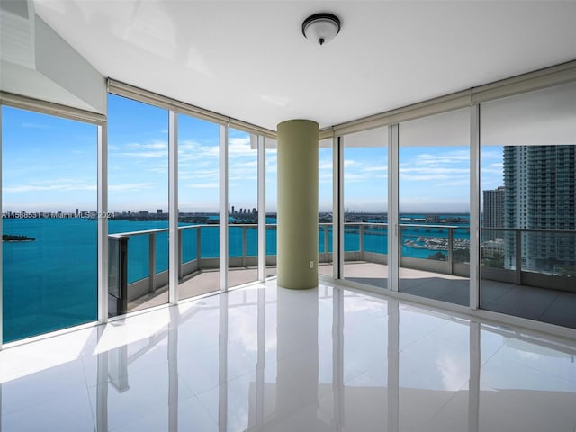 tiled empty room featuring a water view and a wall of windows