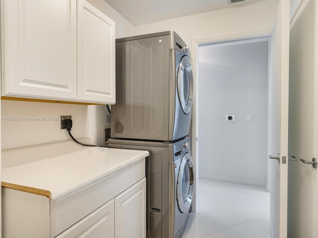 clothes washing area with stacked washer / dryer, light tile patterned flooring, and cabinets