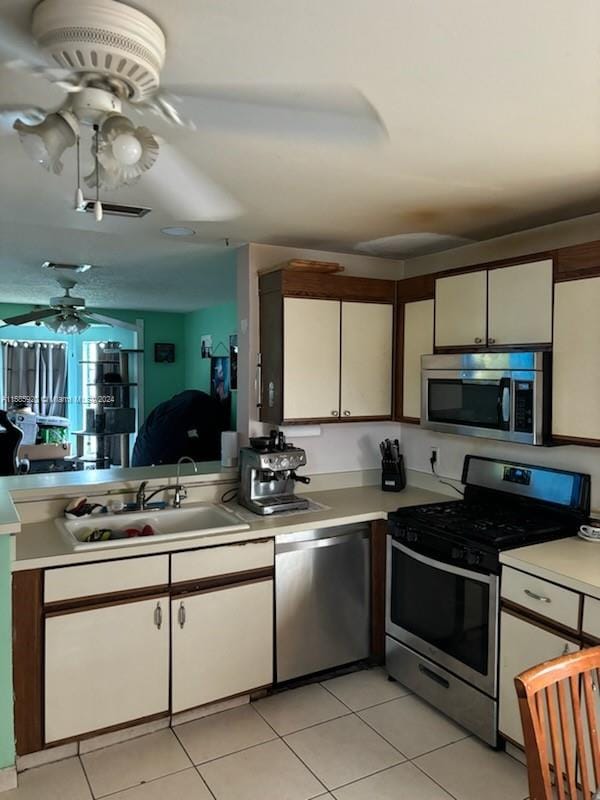 kitchen with light tile patterned floors, white cabinets, ceiling fan, appliances with stainless steel finishes, and sink