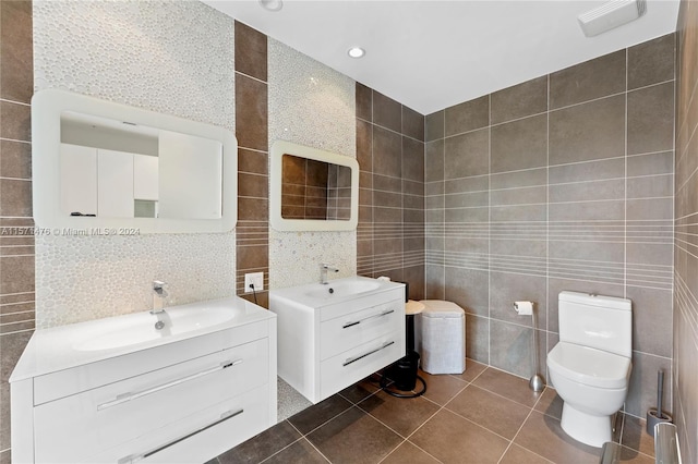 bathroom with dual bowl vanity, tile walls, toilet, and tile floors