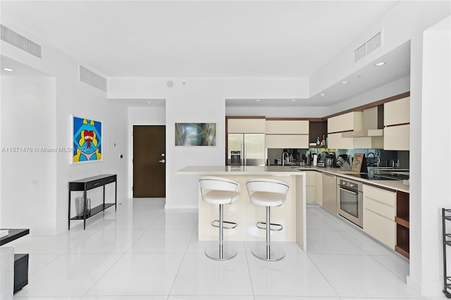 kitchen with appliances with stainless steel finishes, wall chimney exhaust hood, a kitchen bar, and light tile floors