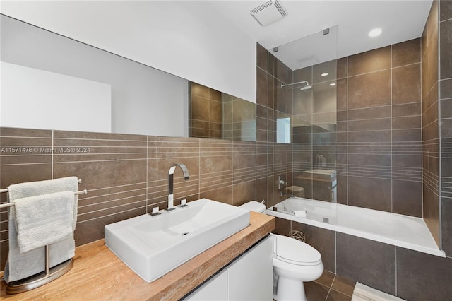 full bathroom with tile walls, toilet, tiled shower / bath combo, and vanity