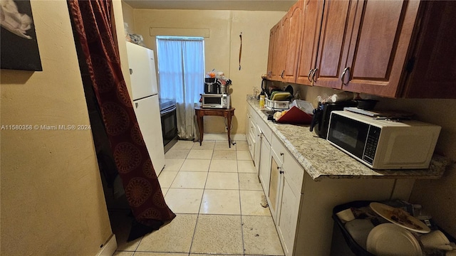 kitchen with light stone countertops, light tile patterned flooring, black stove, and white fridge