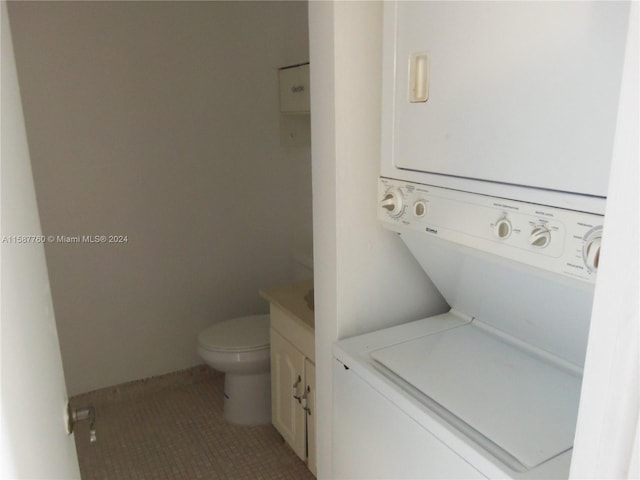 bathroom featuring stacked washer and clothes dryer, tile flooring, vanity, and toilet