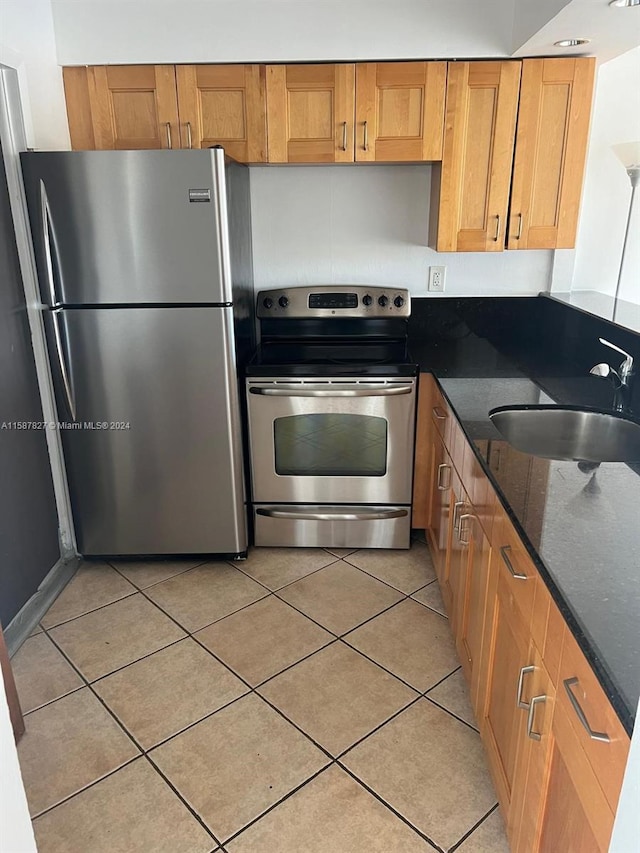 kitchen featuring dark stone countertops, sink, light tile flooring, and appliances with stainless steel finishes