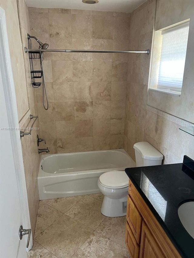 full bathroom with tile flooring, tile walls, tiled shower / bath combo, vanity, and toilet