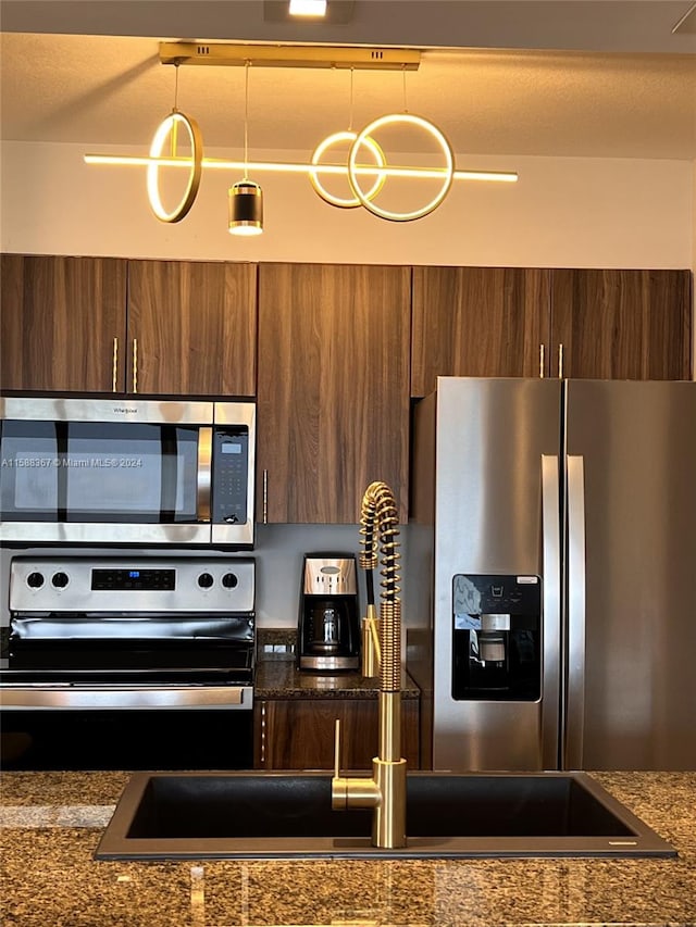 kitchen featuring stainless steel appliances, dark stone countertops, and decorative light fixtures