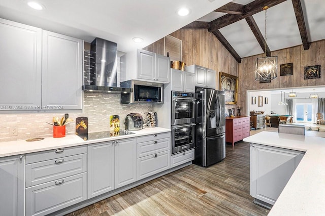 kitchen with wooden walls, light countertops, appliances with stainless steel finishes, wall chimney exhaust hood, and beamed ceiling