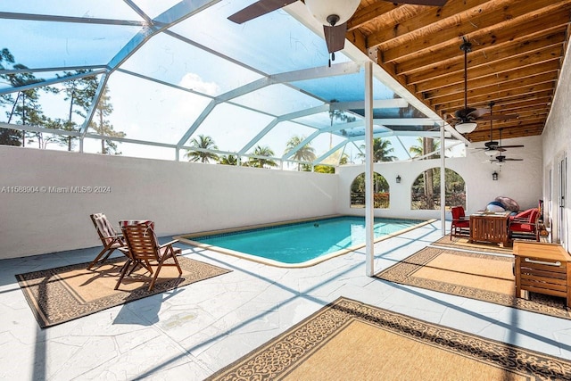 view of swimming pool with glass enclosure, ceiling fan, a fenced in pool, and a patio