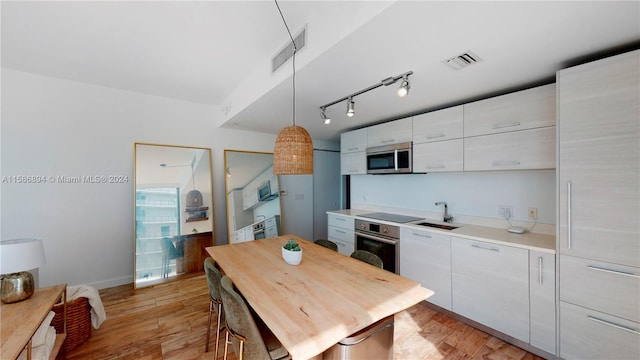 kitchen featuring hanging light fixtures, track lighting, light wood-type flooring, and appliances with stainless steel finishes