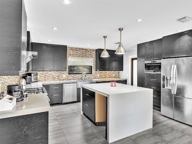 kitchen featuring decorative light fixtures, stainless steel appliances, light countertops, decorative backsplash, and a kitchen island