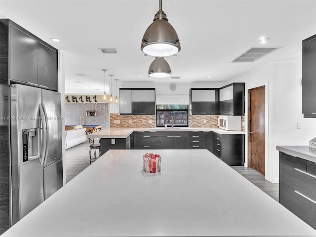 kitchen featuring white microwave, light countertops, modern cabinets, stainless steel fridge, and decorative light fixtures