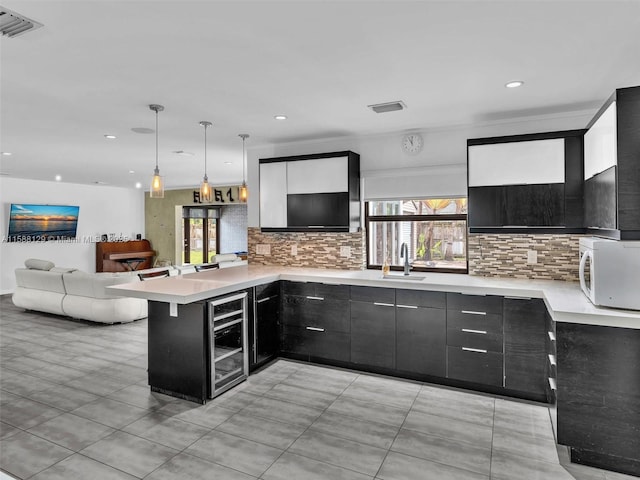 kitchen with light countertops, hanging light fixtures, white microwave, beverage cooler, and a peninsula