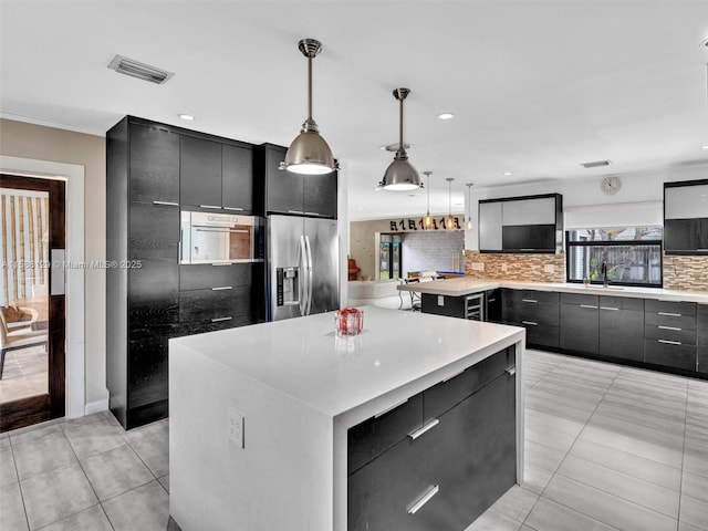 kitchen featuring a kitchen island, hanging light fixtures, light countertops, decorative backsplash, and stainless steel fridge