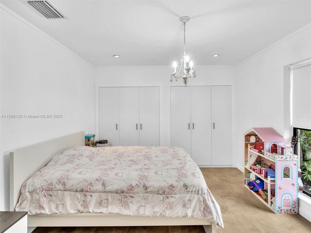 bedroom featuring an inviting chandelier, crown molding, and multiple closets