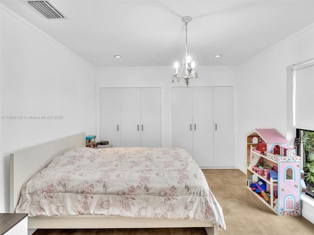 bedroom with a chandelier, ornamental molding, two closets, and visible vents