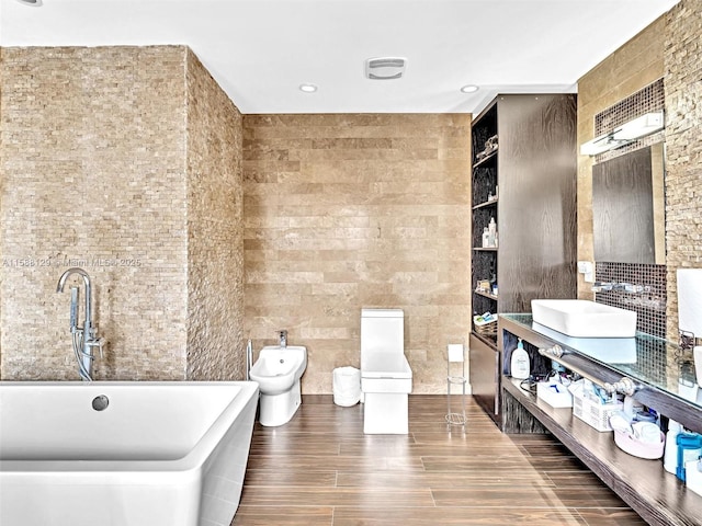 full bathroom featuring a freestanding tub, a sink, tile walls, double vanity, and a bidet