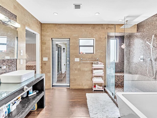 bathroom with vanity, separate shower and tub, hardwood / wood-style floors, and tile walls