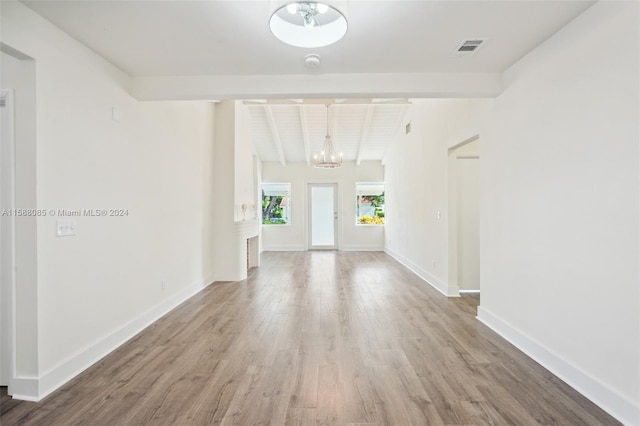 spare room with lofted ceiling with beams, light wood-type flooring, and an inviting chandelier