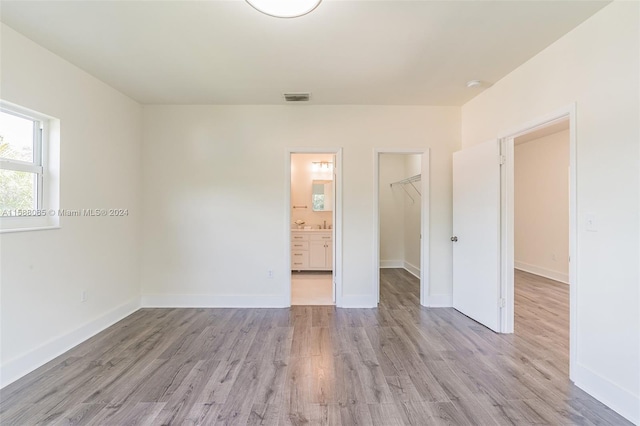 unfurnished bedroom featuring ensuite bath, a closet, light wood-type flooring, and a spacious closet