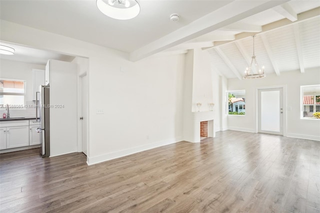 unfurnished living room featuring sink, lofted ceiling with beams, wood-type flooring, and an inviting chandelier