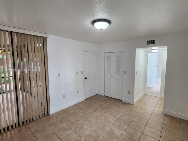 unfurnished bedroom featuring a textured ceiling, a closet, and light tile patterned floors