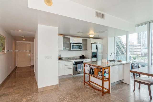 kitchen with light stone countertops, stainless steel appliances, light tile floors, sink, and white cabinetry