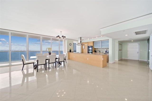 kitchen featuring an inviting chandelier, a water view, backsplash, rail lighting, and light tile floors