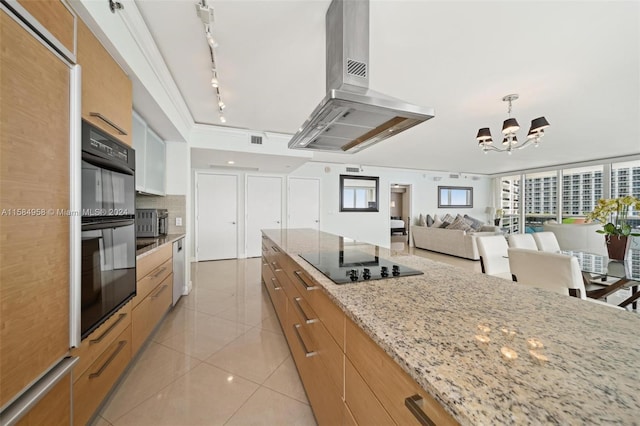 kitchen featuring a notable chandelier, island range hood, black appliances, light stone countertops, and track lighting