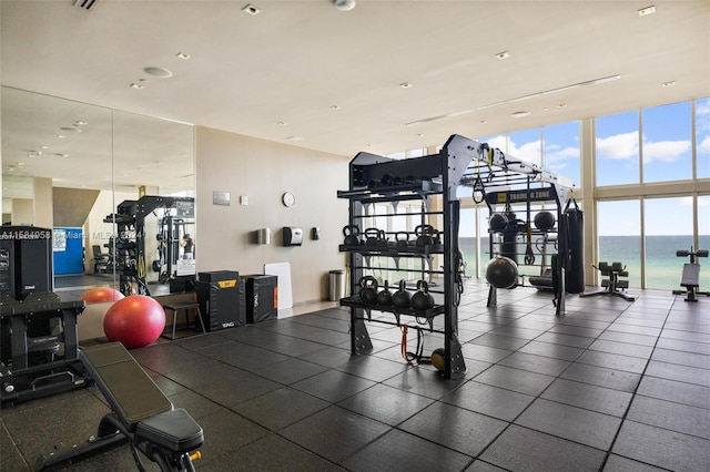 exercise room featuring tile floors, a wall of windows, and a water view