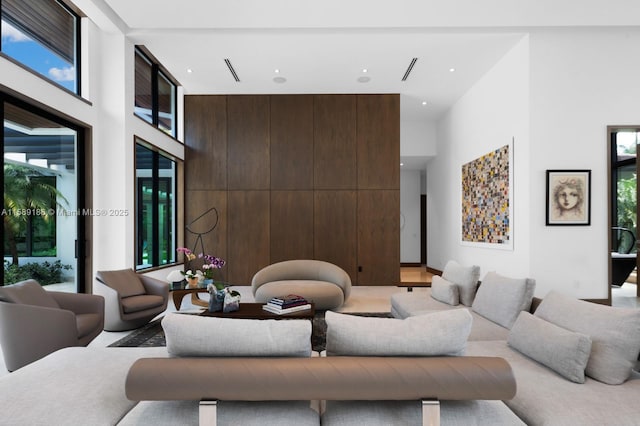 living room featuring a towering ceiling, wooden walls, and a healthy amount of sunlight