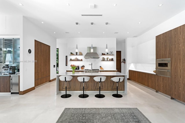 kitchen featuring wall chimney range hood, sink, a breakfast bar, hanging light fixtures, and oven