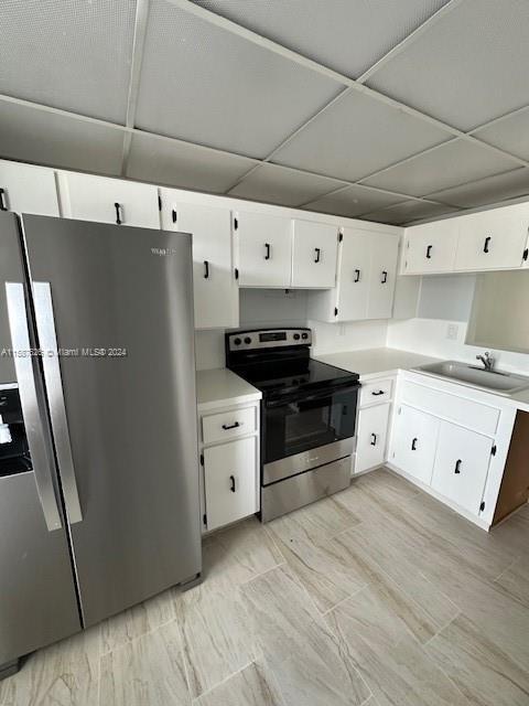 kitchen with stainless steel appliances, white cabinetry, and a drop ceiling