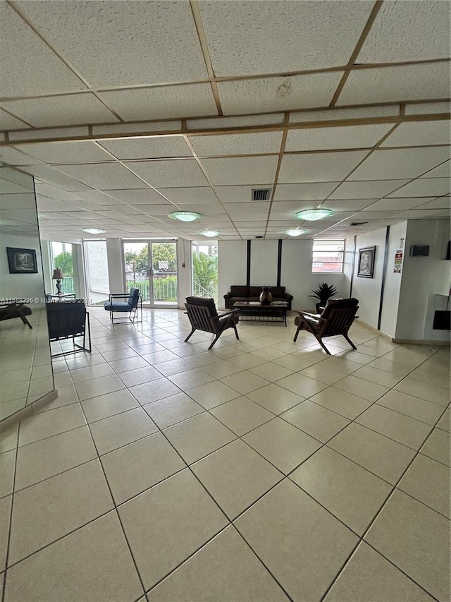 unfurnished living room with a wealth of natural light, light tile floors, and a drop ceiling