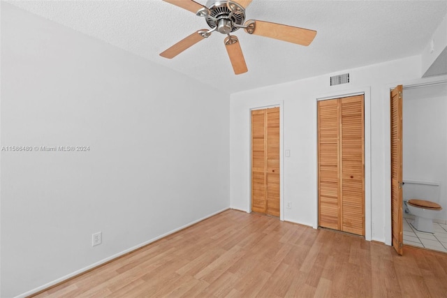 unfurnished bedroom with multiple closets, a textured ceiling, ceiling fan, and light tile floors