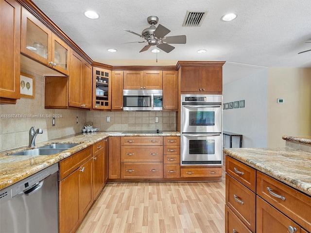 kitchen with decorative backsplash, light stone countertops, stainless steel appliances, sink, and light hardwood / wood-style flooring