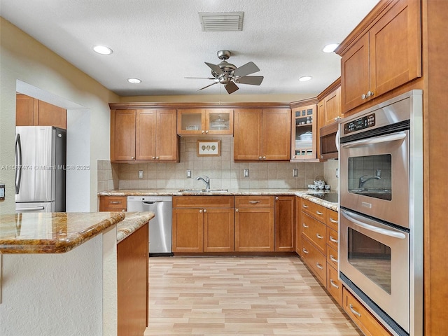 kitchen featuring glass insert cabinets, visible vents, appliances with stainless steel finishes, and brown cabinets