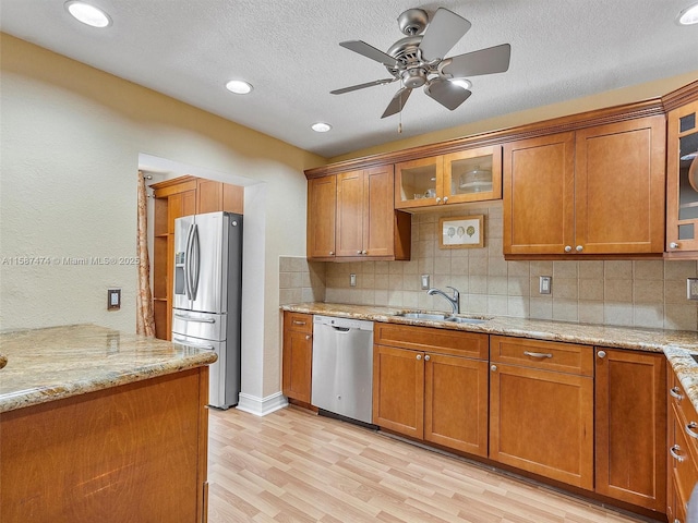 kitchen with light wood-style flooring, light stone countertops, stainless steel appliances, brown cabinets, and glass insert cabinets