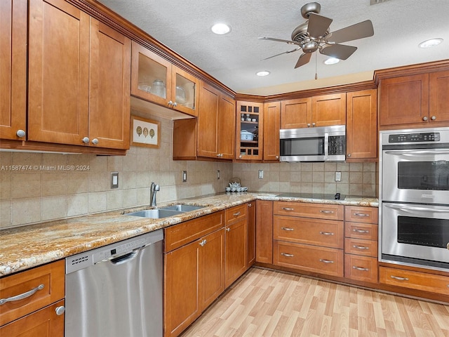 kitchen with sink, stainless steel appliances, light stone counters, backsplash, and light wood-type flooring