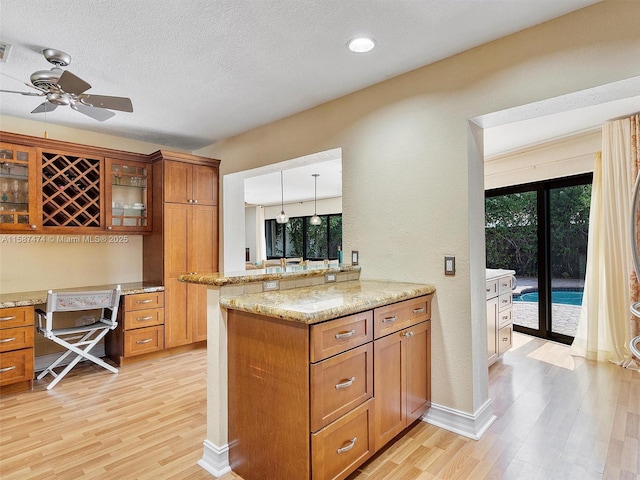 kitchen featuring a peninsula, glass insert cabinets, brown cabinetry, and pendant lighting