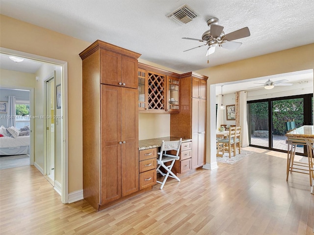 kitchen with ceiling fan, built in desk, light stone countertops, a textured ceiling, and light hardwood / wood-style floors