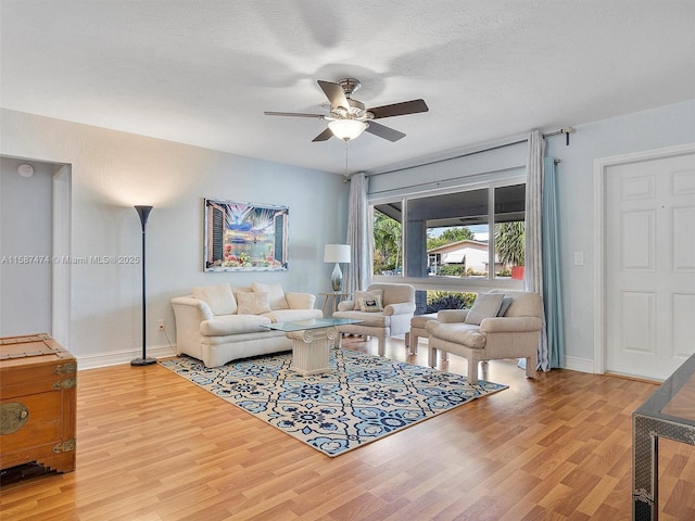 living area with ceiling fan, a textured ceiling, baseboards, and wood finished floors