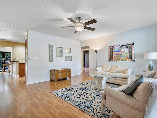 living area with a textured ceiling, baseboards, a ceiling fan, and light wood-style floors