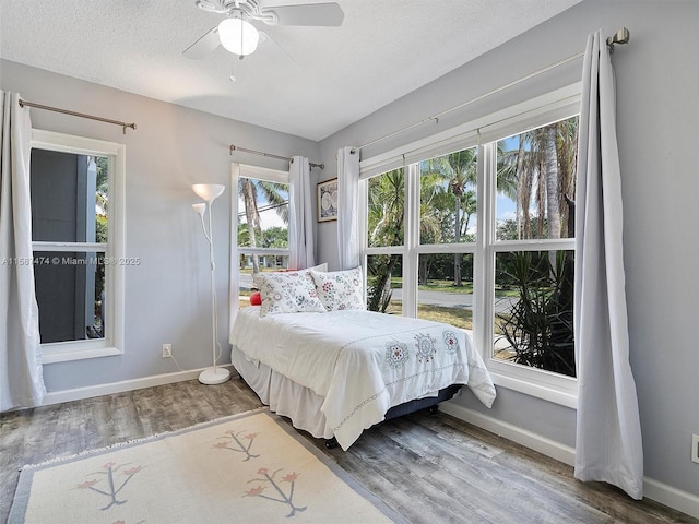 bedroom featuring a ceiling fan, a textured ceiling, baseboards, and wood finished floors